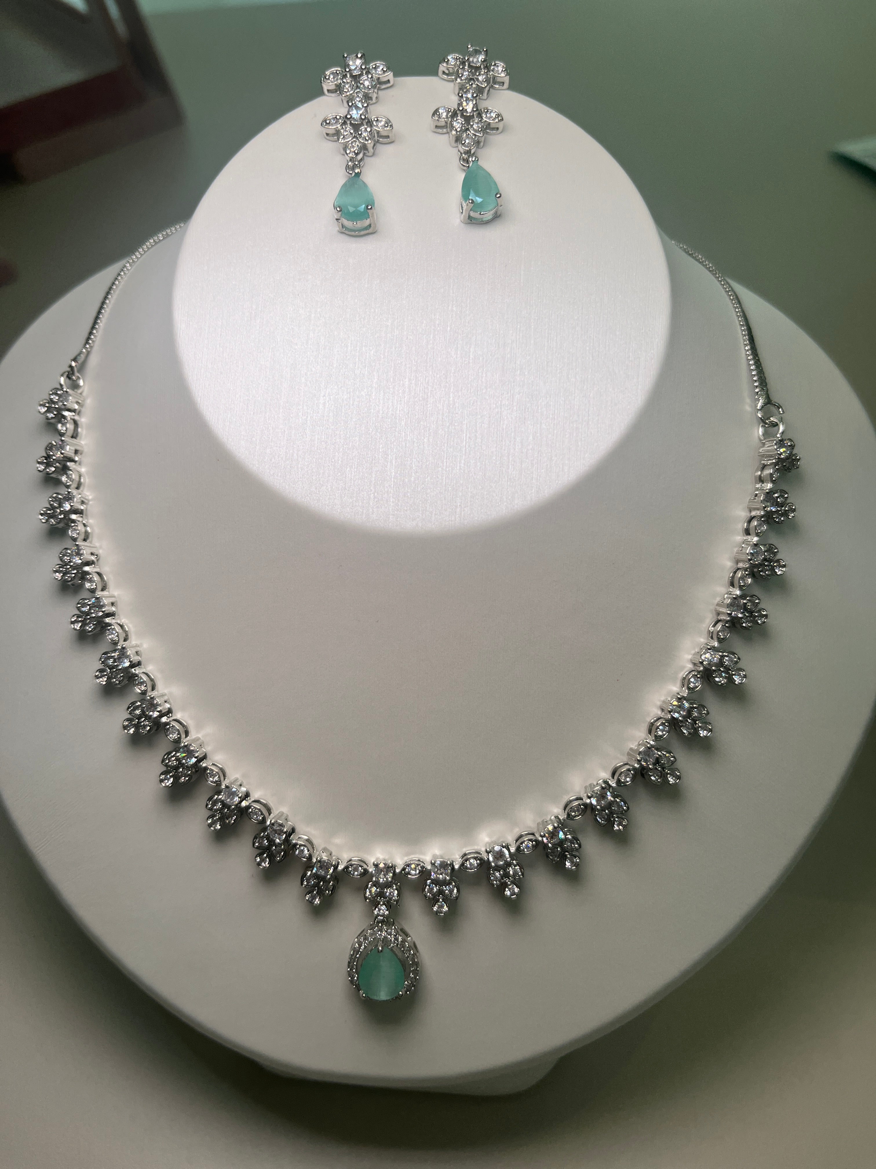 A necklace and earrings set featuring a teardrop-shaped gemstone centerpiece with a silver-tone finish, displayed on a mannequin bust.
