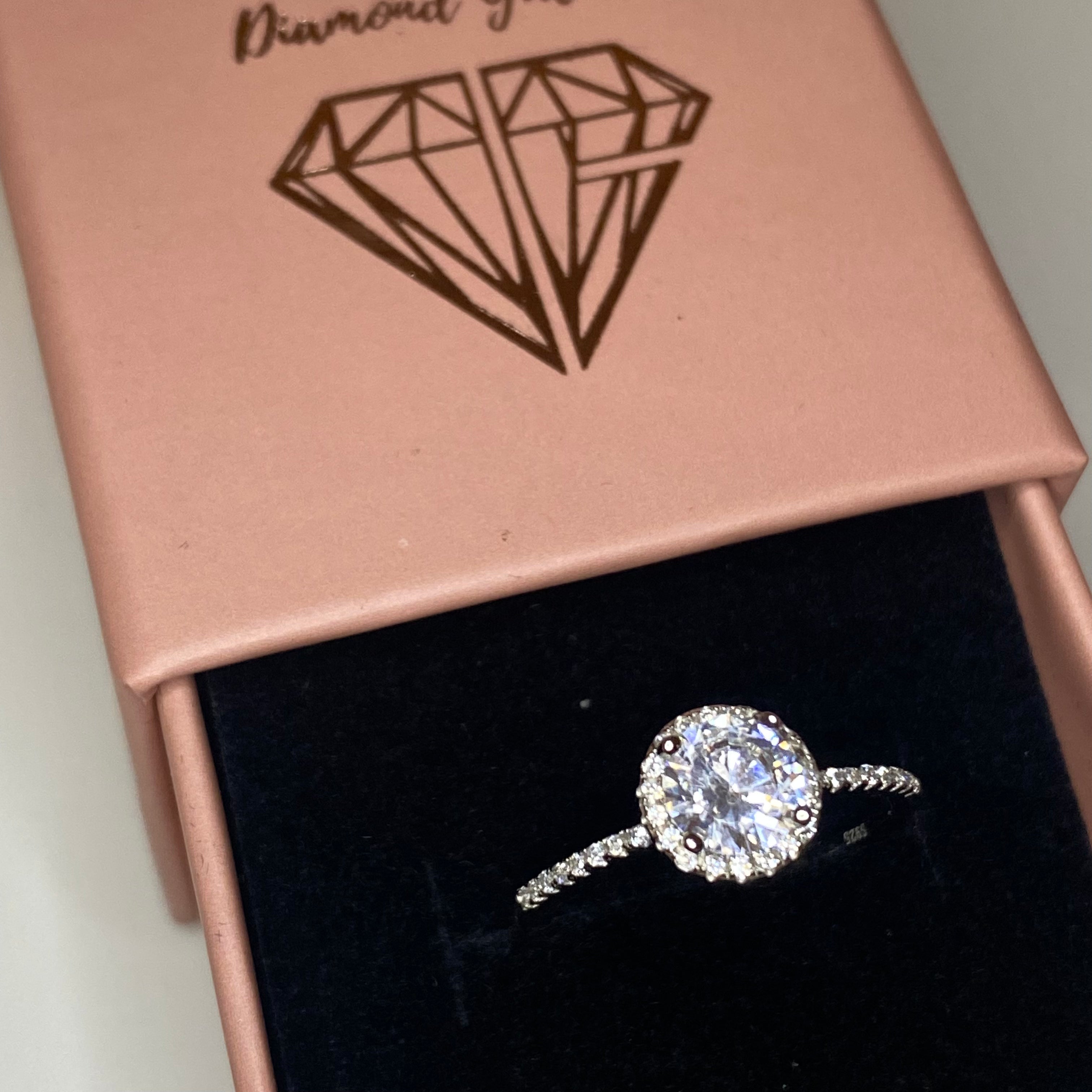 A sterling silver engagement ring with a central cubic zirconia stone surrounded by smaller clear stones, featuring a classic six-prong setting.