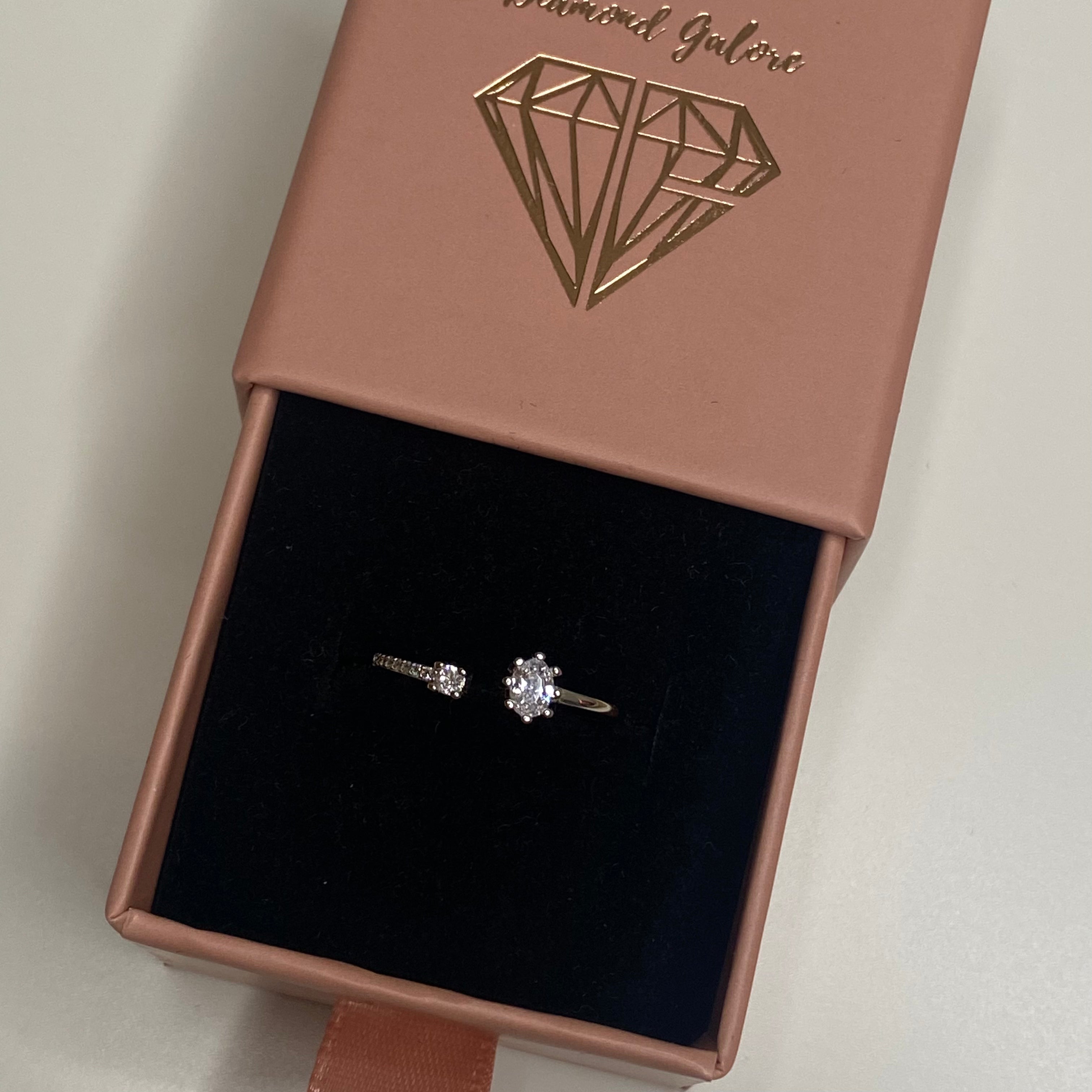 Adjustable silver ring with a clear, ornate design around the central stone placed in a box.