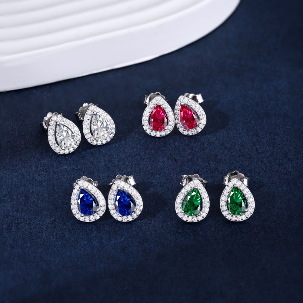 Four different pairs of pear-shaped stud earrings with red, green, blue, and white main stones and clear accent stones set in sterling silver bands.