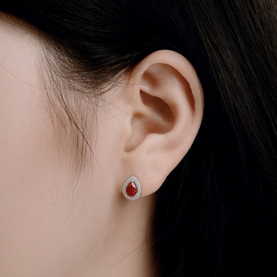 A pear-shaped stud earring with red main stone and clear accent stones set in sterling silver bands.