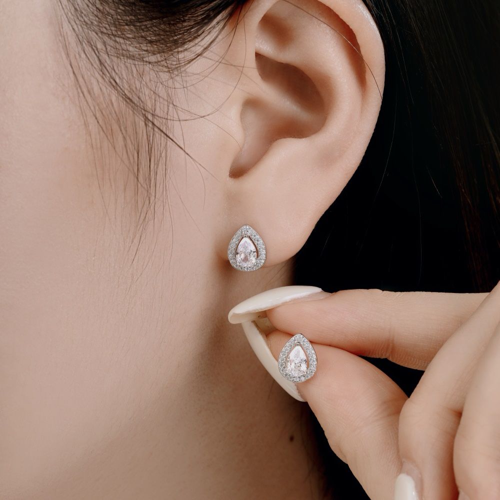 A pair of pear-shaped stud earrings with white main stones and clear accent stones set in sterling silver bands.