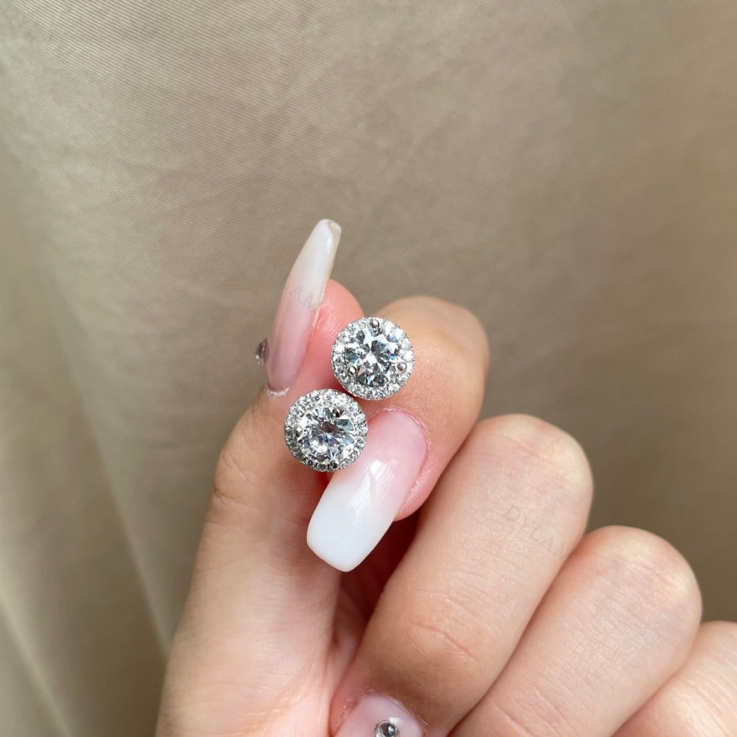 A pair of rhodium-plated stud earrings with a clear, zirconia main stone set in a small circle design.