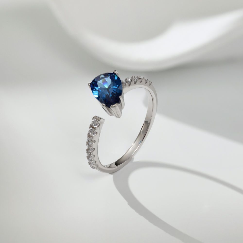 A blue pear-shaped zircon ring with a white silver band and small clear crystals set around the top edge.