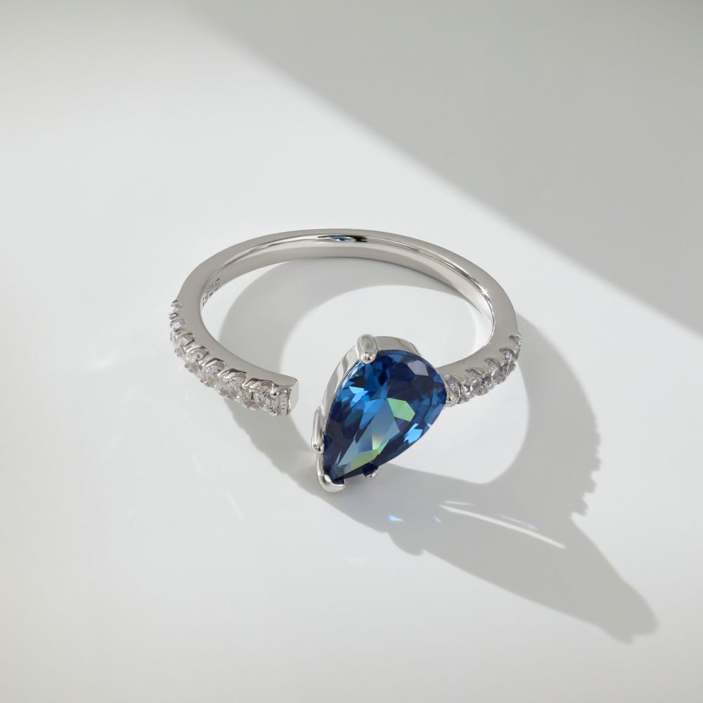 A blue pear-shaped zircon ring with a white silver band and small clear crystals set around the top edge.