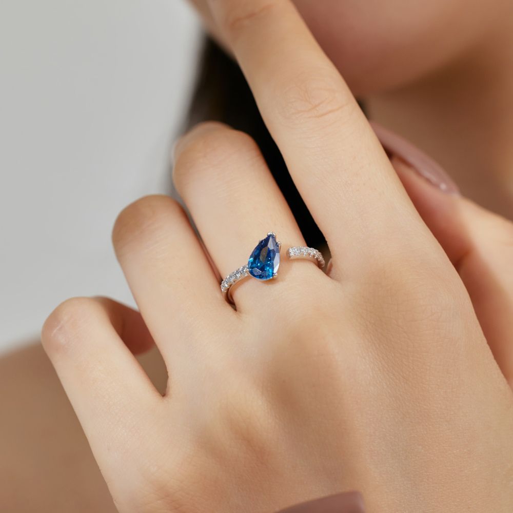 A blue pear-shaped zircon ring with a white silver band and small clear crystals set around the top edge.
