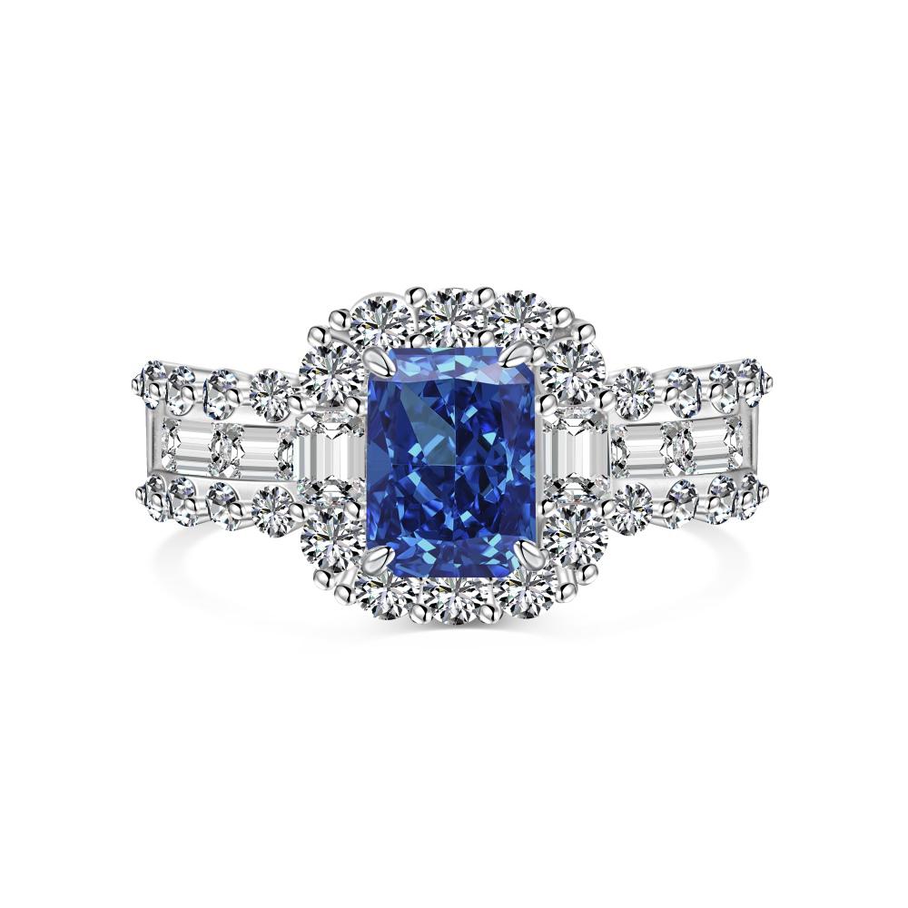 A blue rectangular radiant cut CZ ring with a halo of smaller clear stones around it, set against a white background