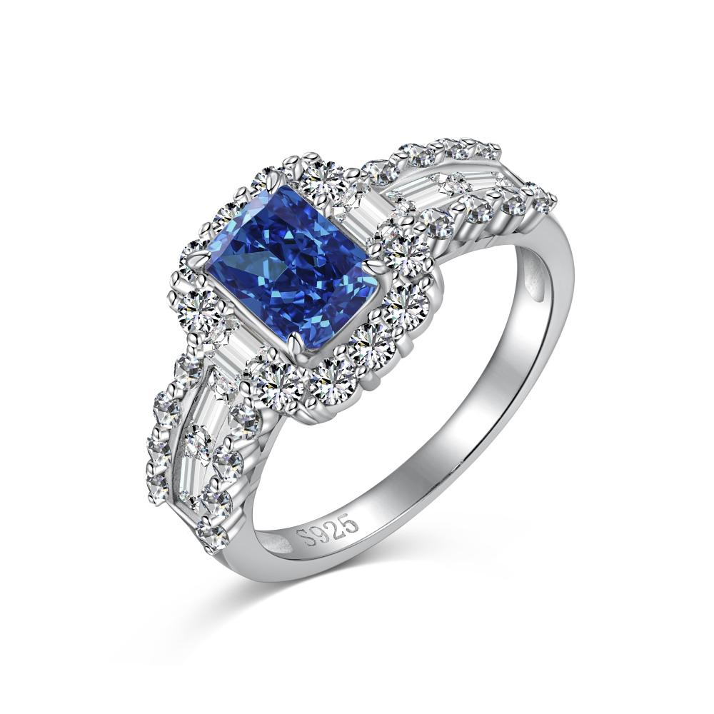 A blue rectangular radiant cut CZ ring with a halo of smaller clear stones around it, set against a white background