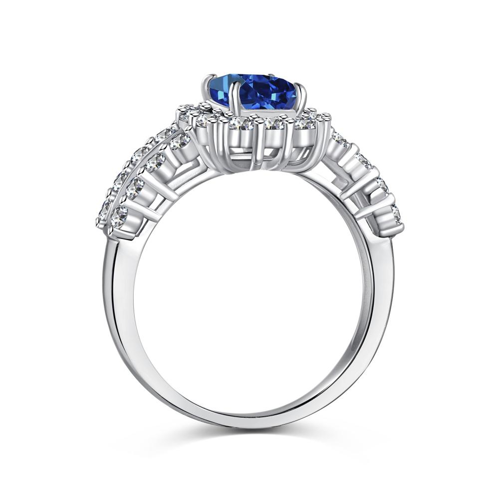 A blue rectangular radiant cut CZ ring with a halo of smaller clear stones around it, set against a white background