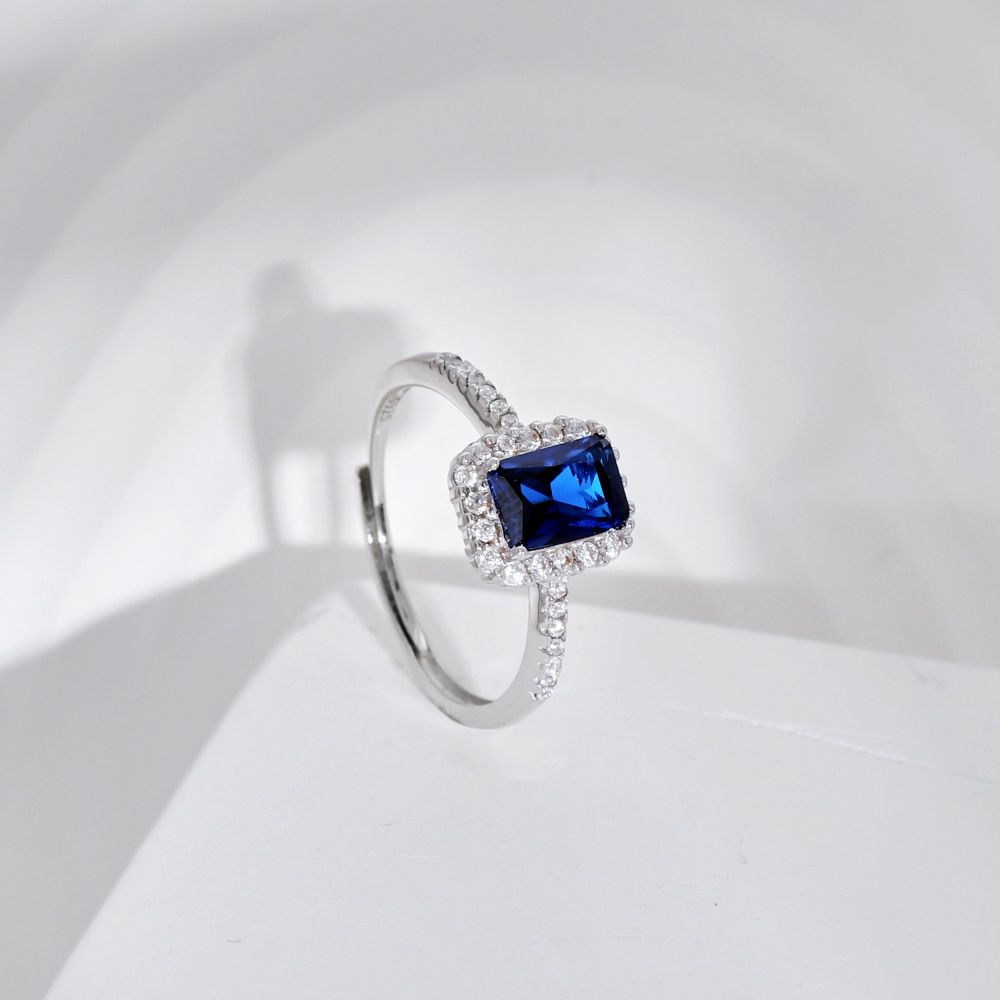 A rectangular-shaped royal blue sapphire ring with a metallic band and small clear stones set around it.