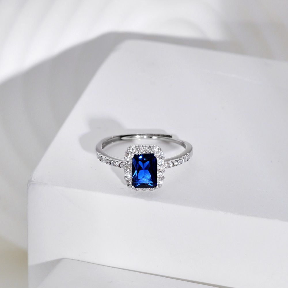 A rectangular-shaped royal blue sapphire ring with a metallic band and small clear stones set around it.