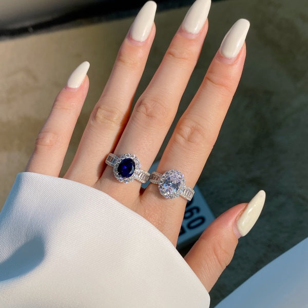 A pair of elegant sterling silver rings featuring an oval white and oval blue zircon stone with smaller clear stones around it, showcasing a traditional Indian royalty-inspired design.