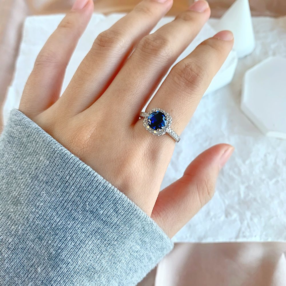 An elegant sterling silver ring featuring a round blue zircon stone with smaller clear stones around it, showcasing an inspired design.