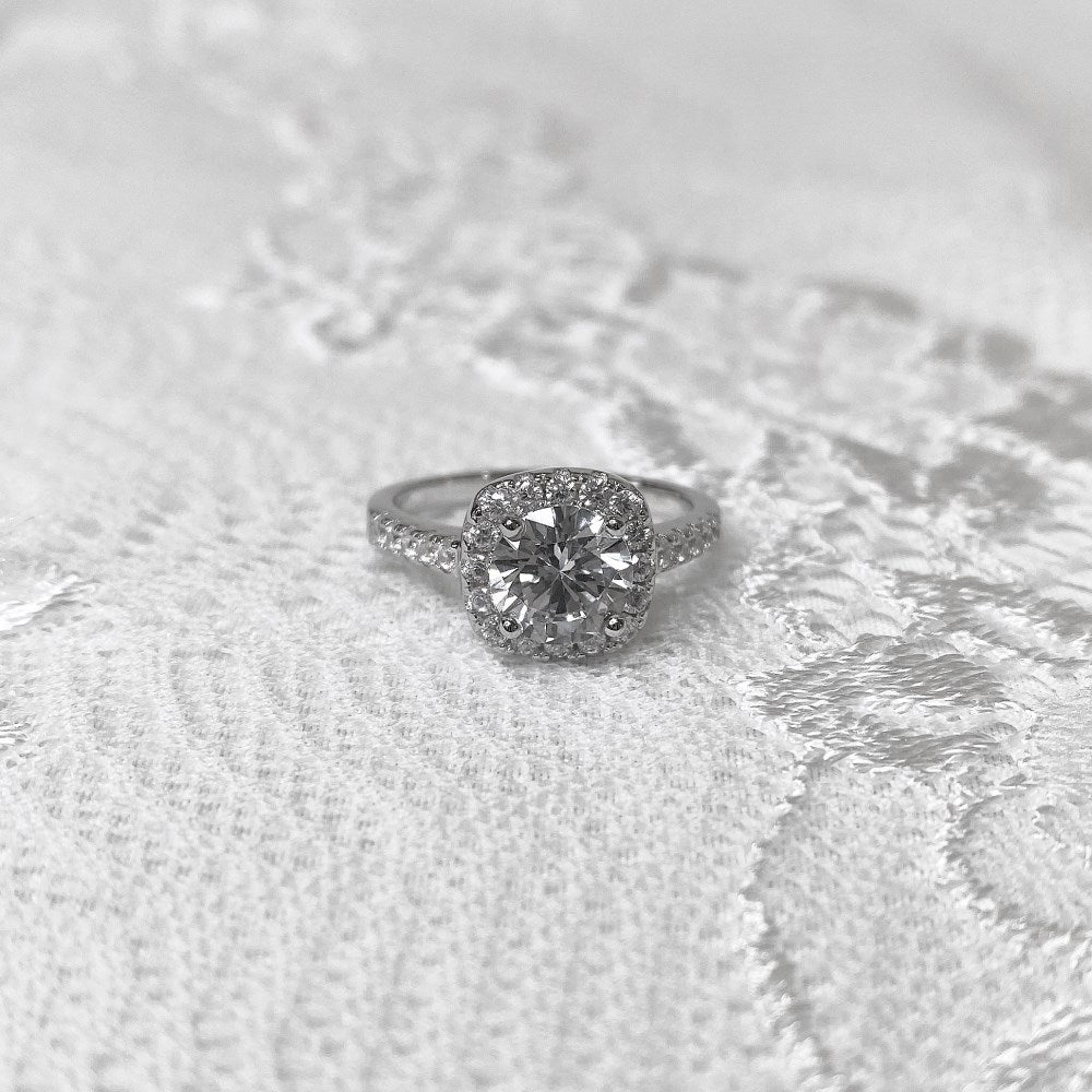 An elegant sterling silver ring featuring a round clear zircon stone with smaller clear stones around it, showcasing an inspired design.