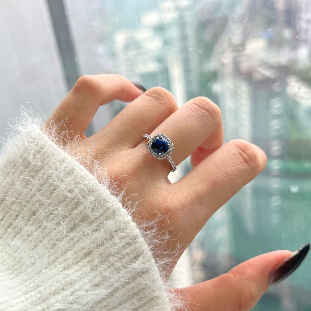 An elegant sterling silver ring featuring a round blue zircon stone with smaller clear stones around it, showcasing an inspired design.