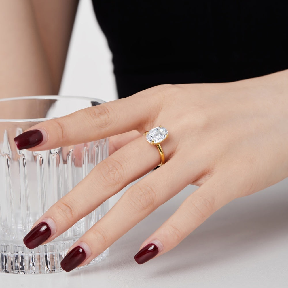 A gold-colored band solitaire ring with a large oval-shaped clear stone