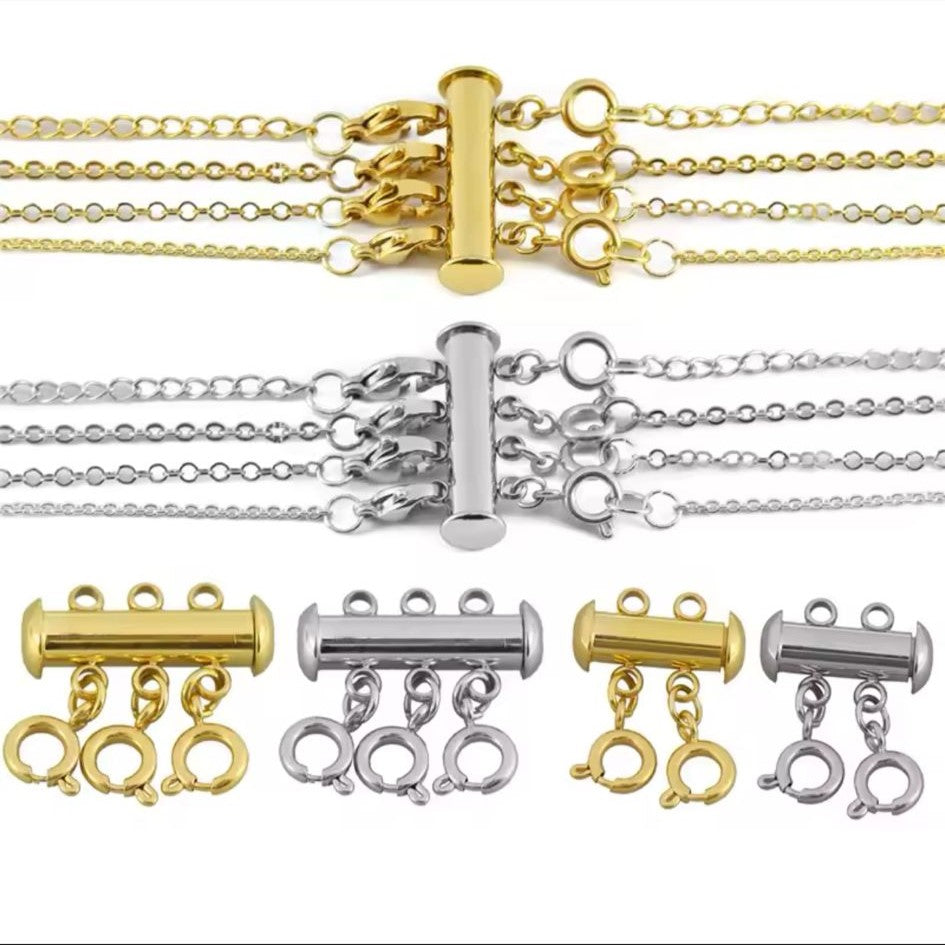 A collection of 18K gold plated triple necklace layering clasp with a gold and silver color option, featuring a cylindrical body with three looped chains extending from the bottom.