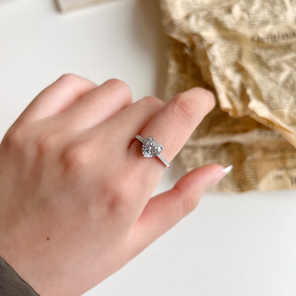 A heart-shaped 5A CZ silver ring with big and small white stones on the band, displayed against a white background.
