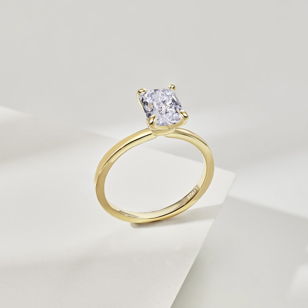 A gold band ring with a single rectangle-shaped clear stone set in a metallic setting.