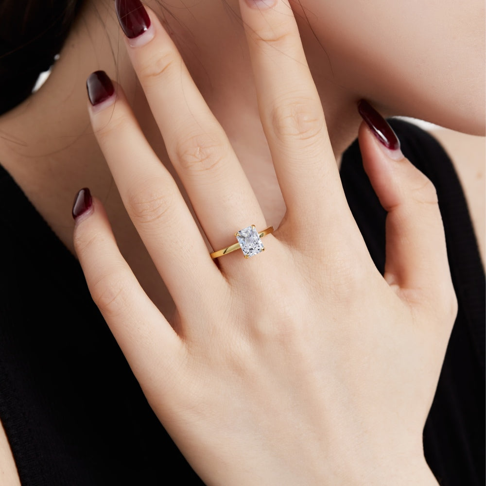 A gold band ring with a single rectangle-shaped clear stone set in a metallic setting displayed over a women's hand.
