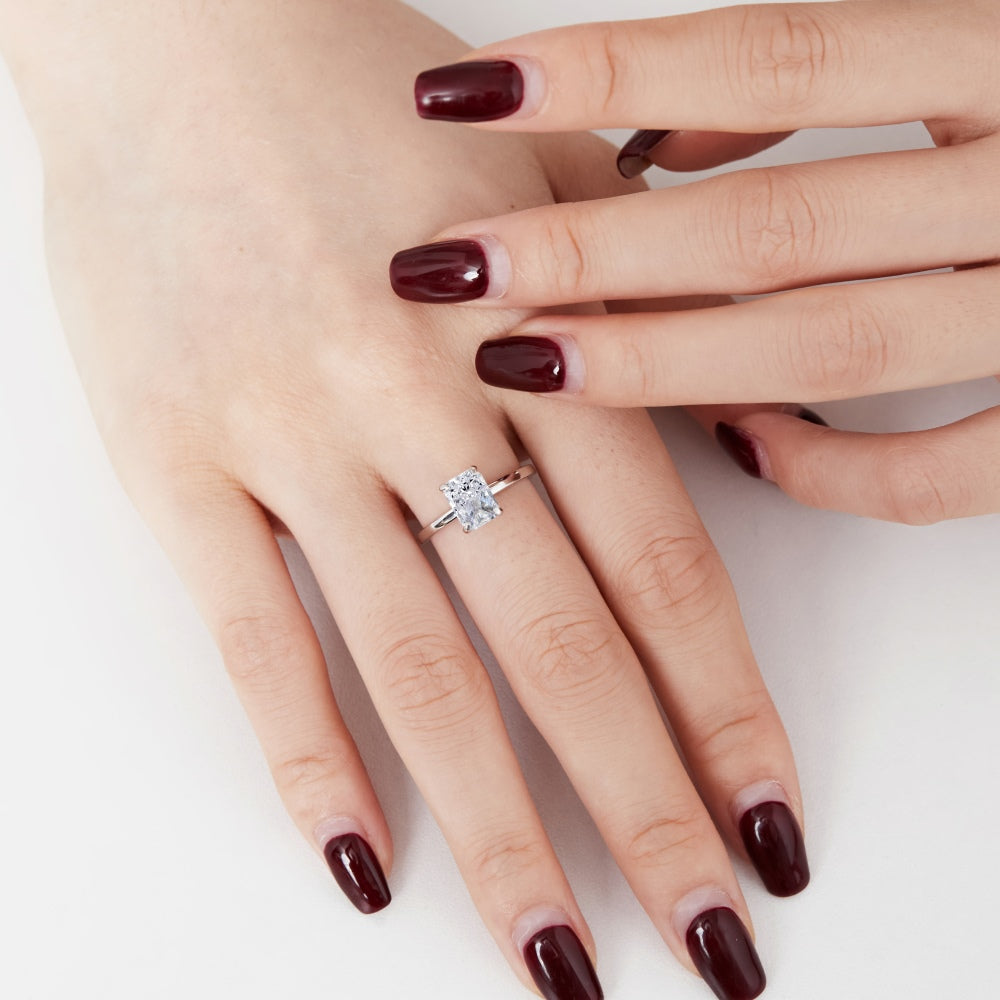 A silver band ring with a single rectangle-shaped clear stone set in a metallic setting on a women's hand.