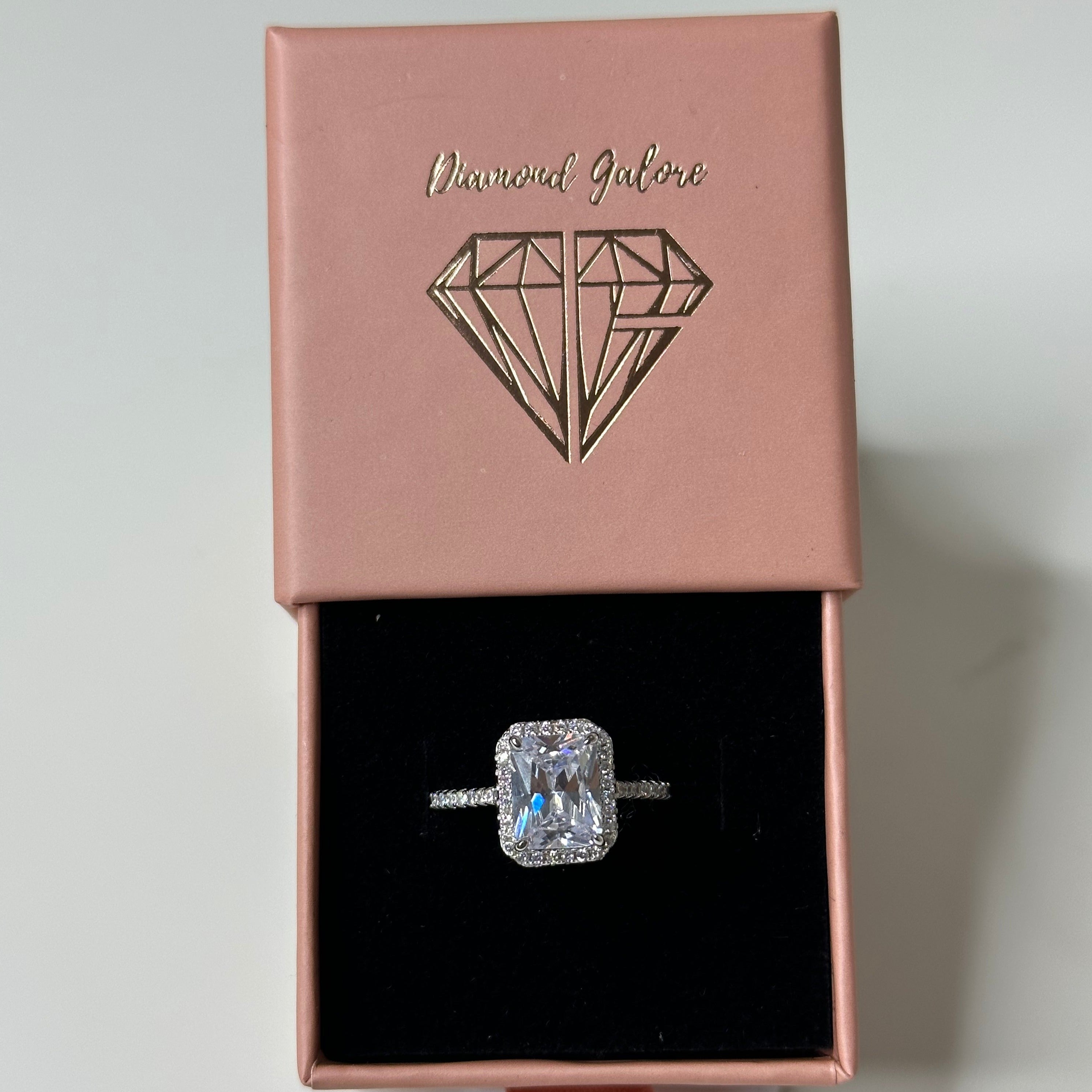 A 3.0 ct Aura Rectangle Radiant Ring with a white gold band and a clear, rectangular main stone surrounded by smaller round stones.