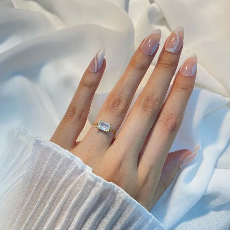 A gold chain ring with gemstone design on a female's hand over a white background