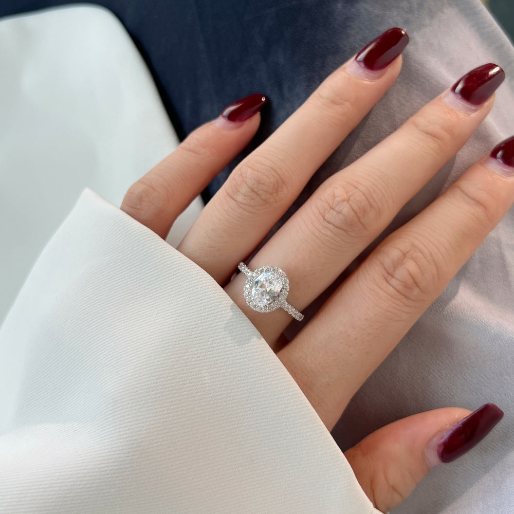 An oval halo ring with a main stone size of 6mm by 8mm, set in a white silver band, surrounded by smaller stones.