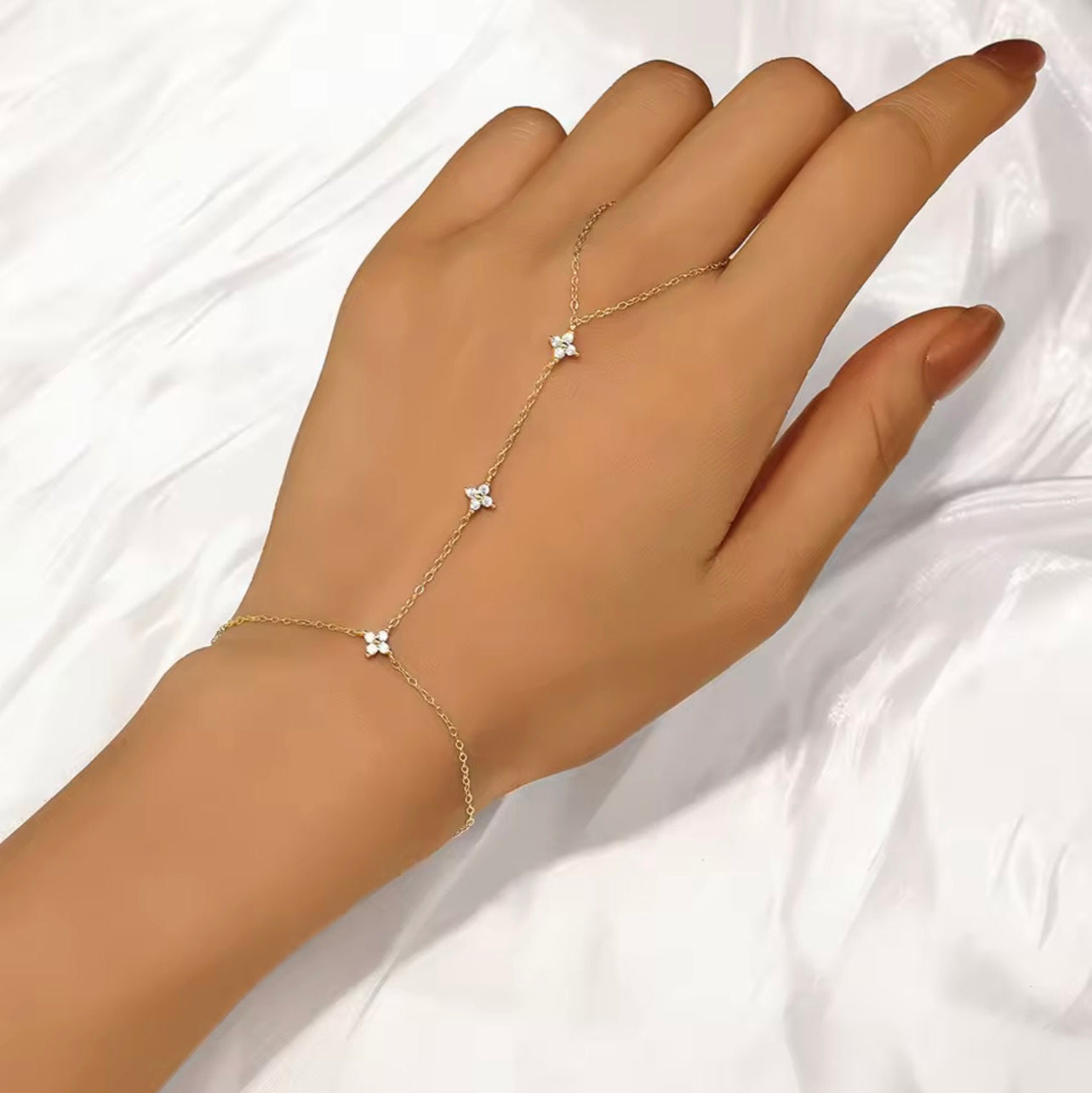 Gold chain bracelet with star-shaped charms on a hand against a white fabric background