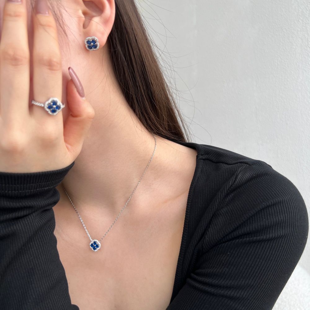 A silver necklace, ring and earring with a clover-shaped pendant adorned with blue cubic zirconia stones.