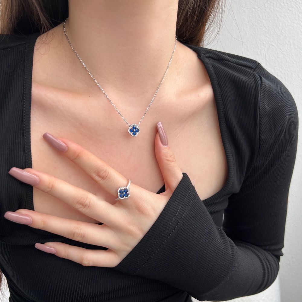 A silver necklace and ring with a clover-shaped pendant adorned with blue cubic zirconia stones.