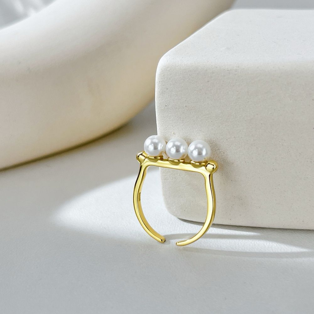 An adjustable ring with 925 sterling silver band and gold plating, featuring three white shell pearls aligned in a row.