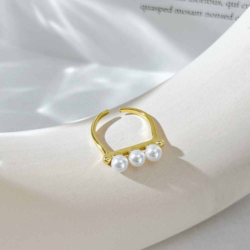 An adjustable ring with 925 sterling silver band and gold plating, featuring three white shell pearls aligned in a row.