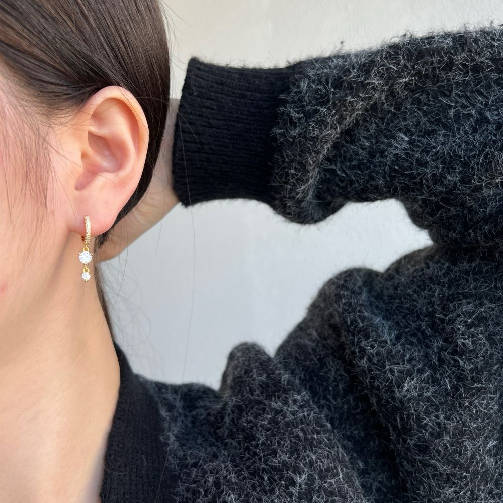 A gold-plated hoop earring with drop-shaped setting containing cubic zirconia stone.