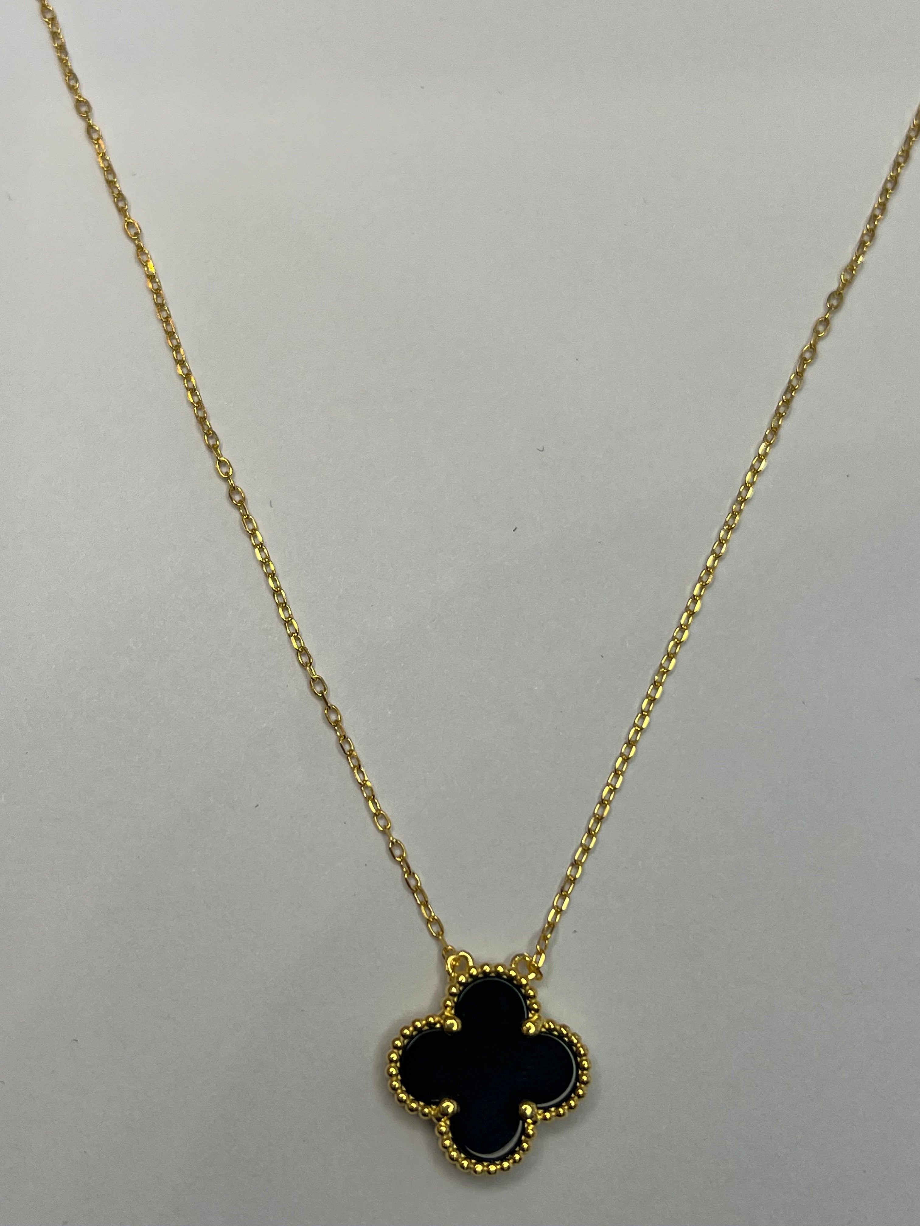 Gold necklace with a black clover-shaped pendant on a light gray background