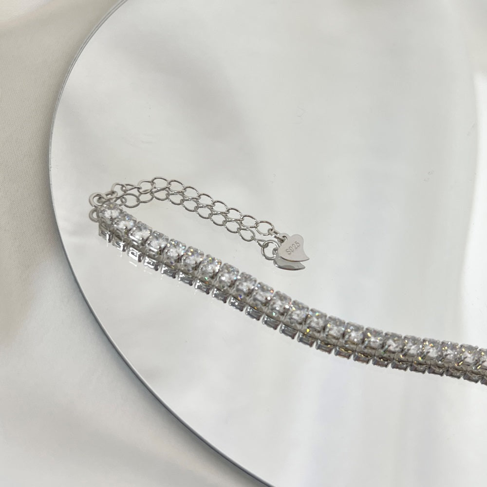 A sterling silver tennis bracelet with silver accents and cubic zirconia stones, featuring a clasp closure.