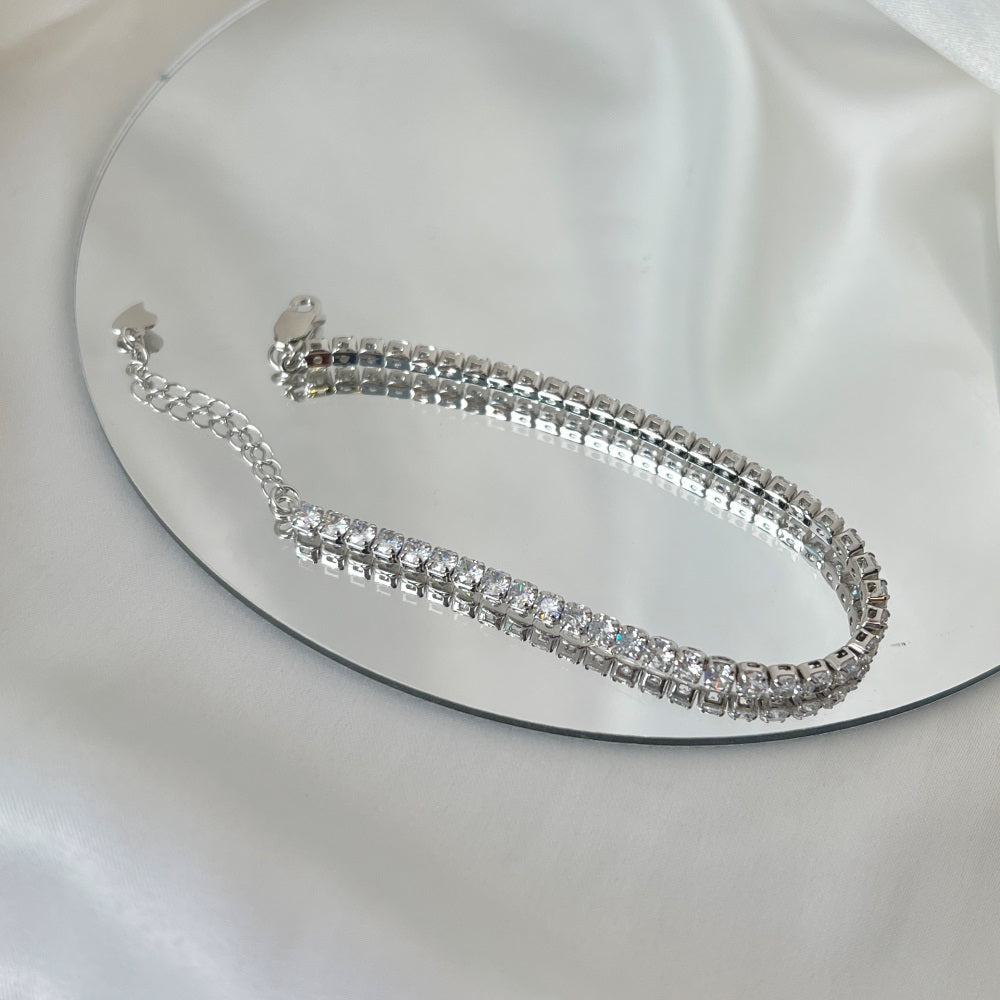 A sterling silver tennis bracelet with silver accents and cubic zirconia stones, featuring a clasp closure.