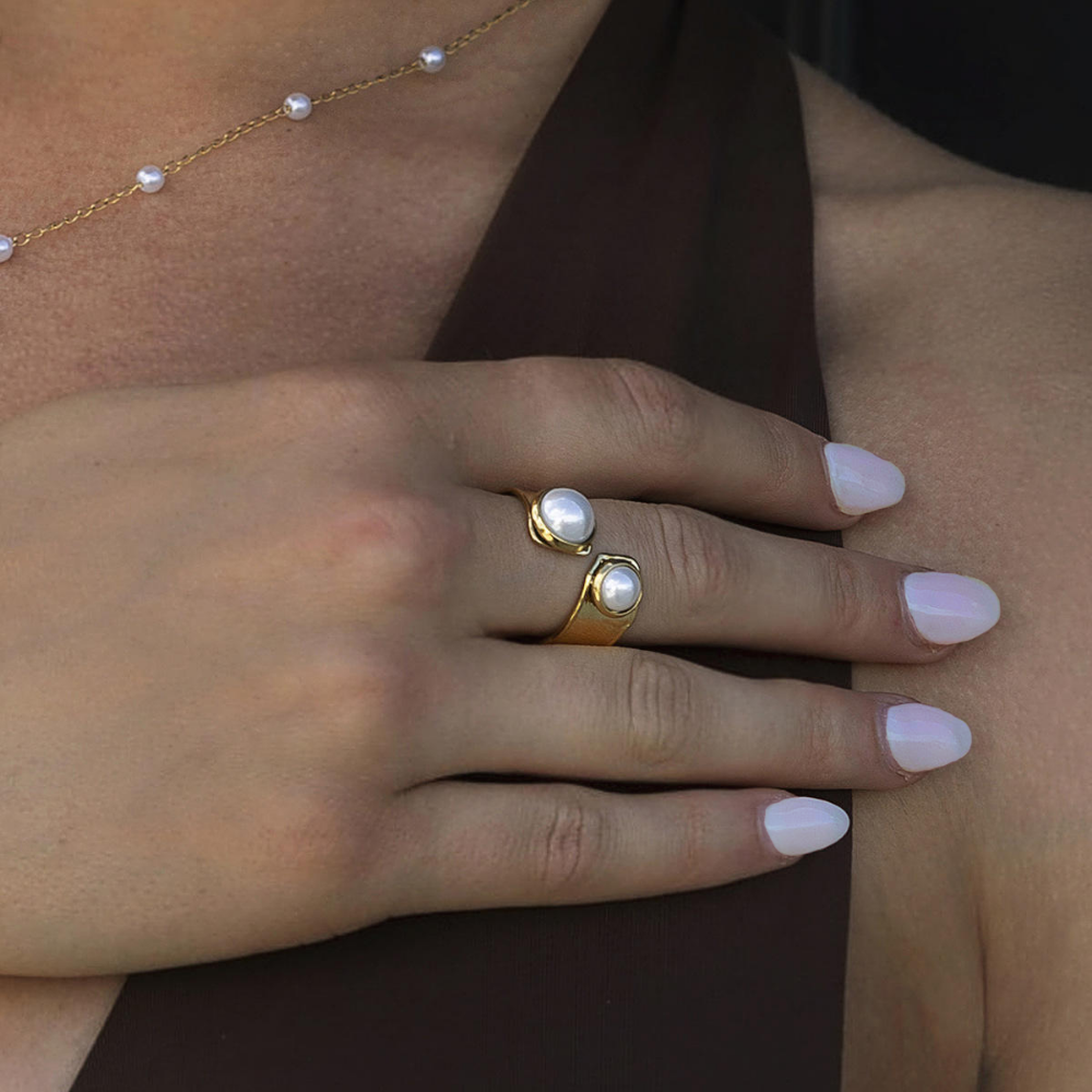 Close-up of a hand wearing a gold ring with a pearl on a dark background