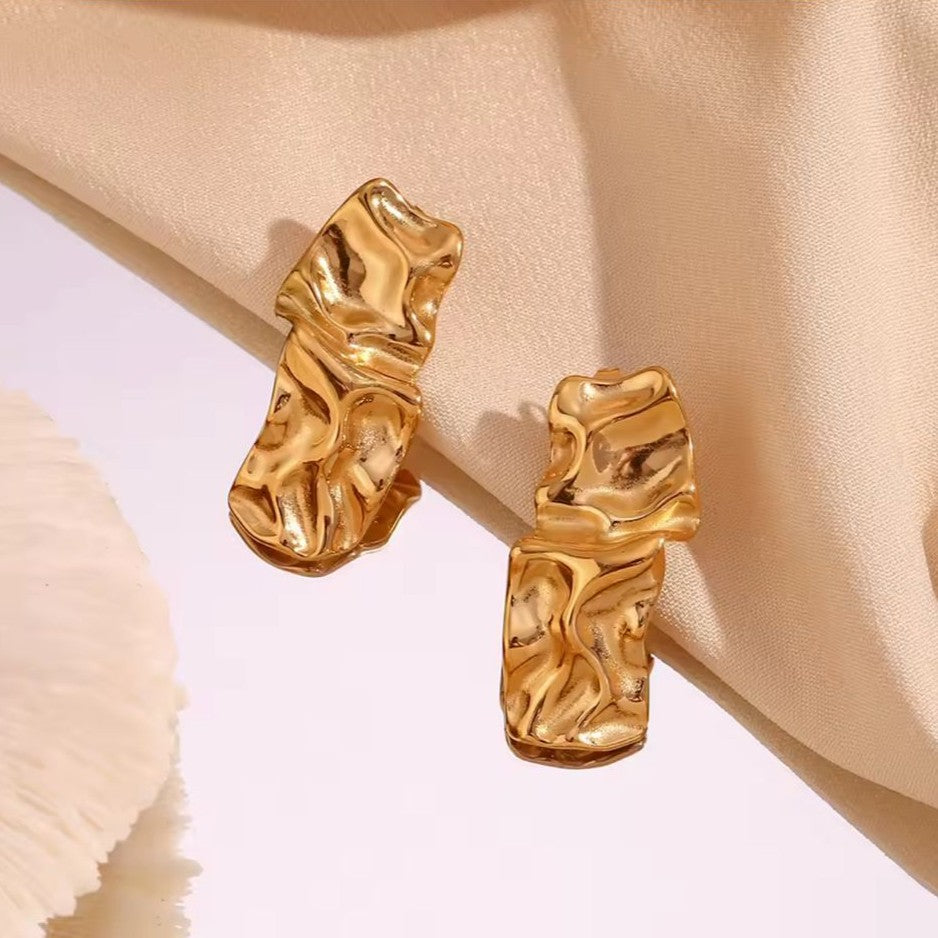 Gold earrings with a marble textured design on a beige fabric background