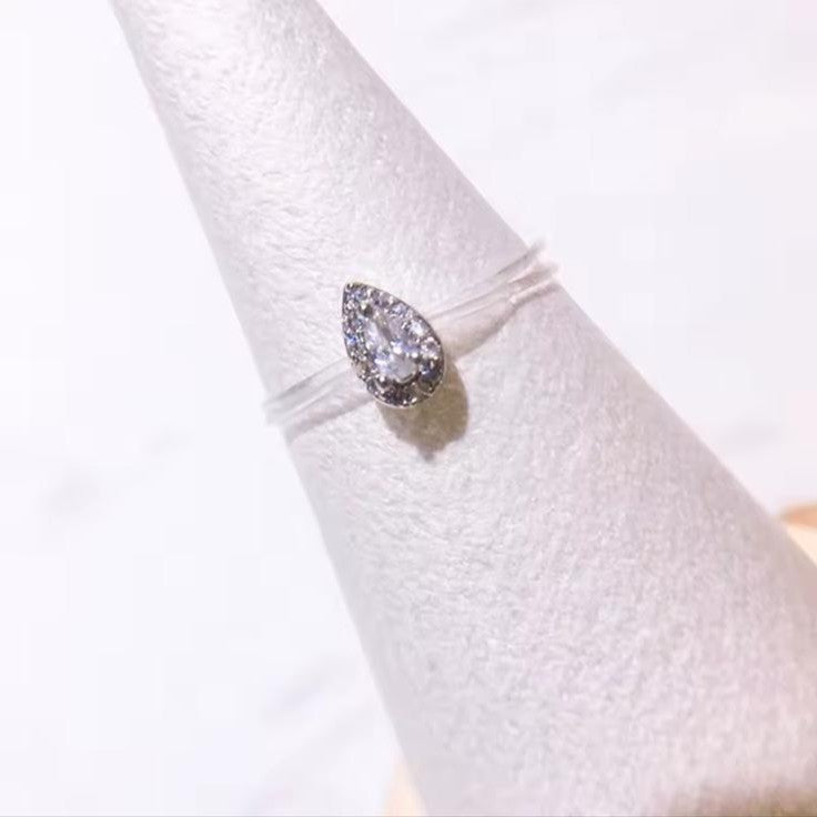 Pear-shaped diamond ring on a clear stand with a white background