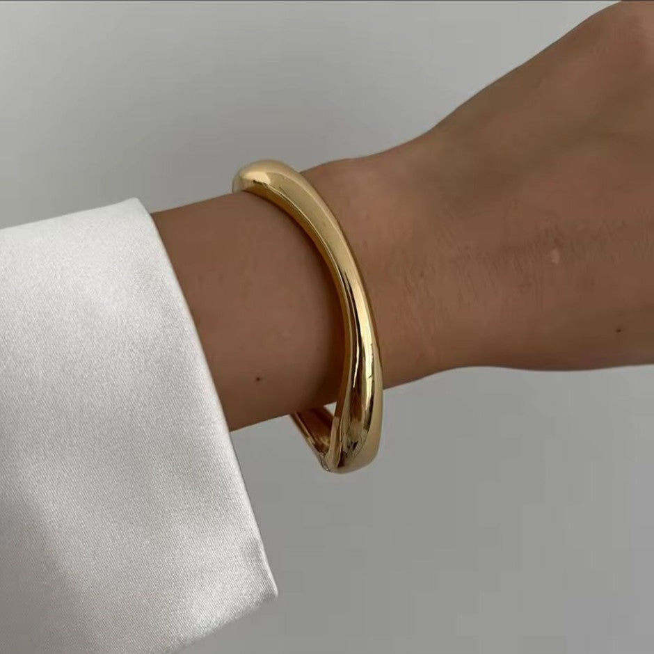 Gold bracelet on a wrist with a plain background
