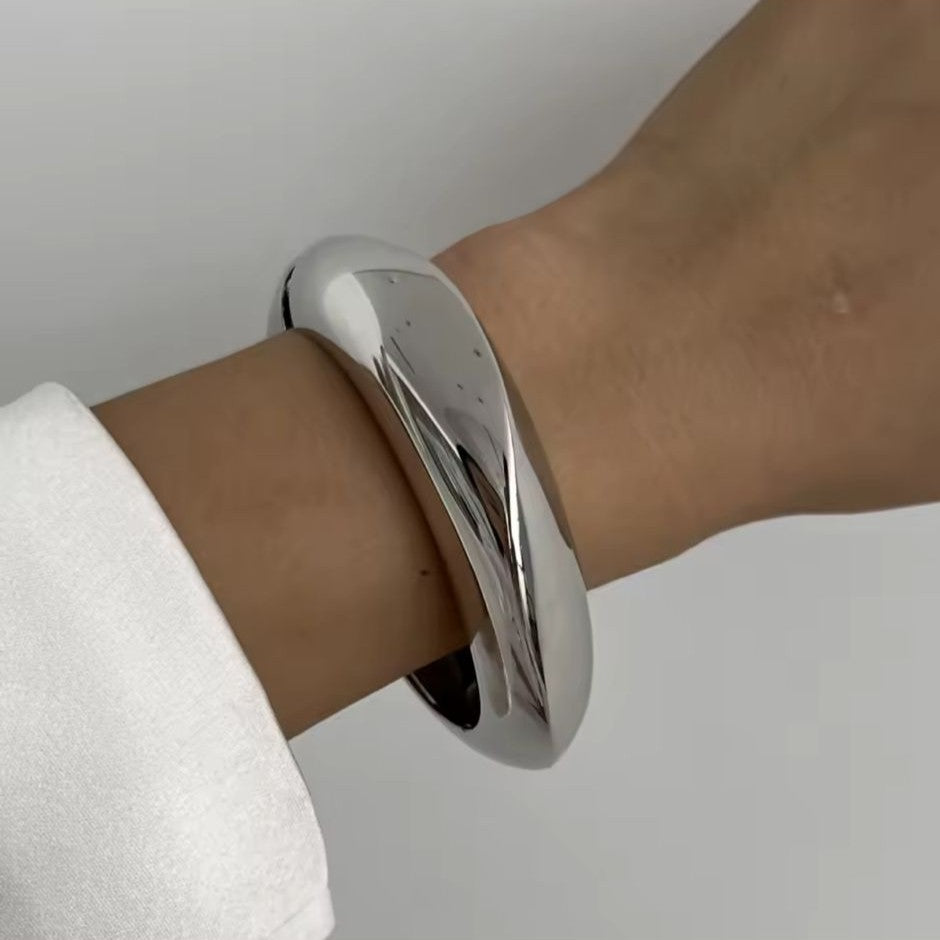 Silver bangle on a wrist with a plain background