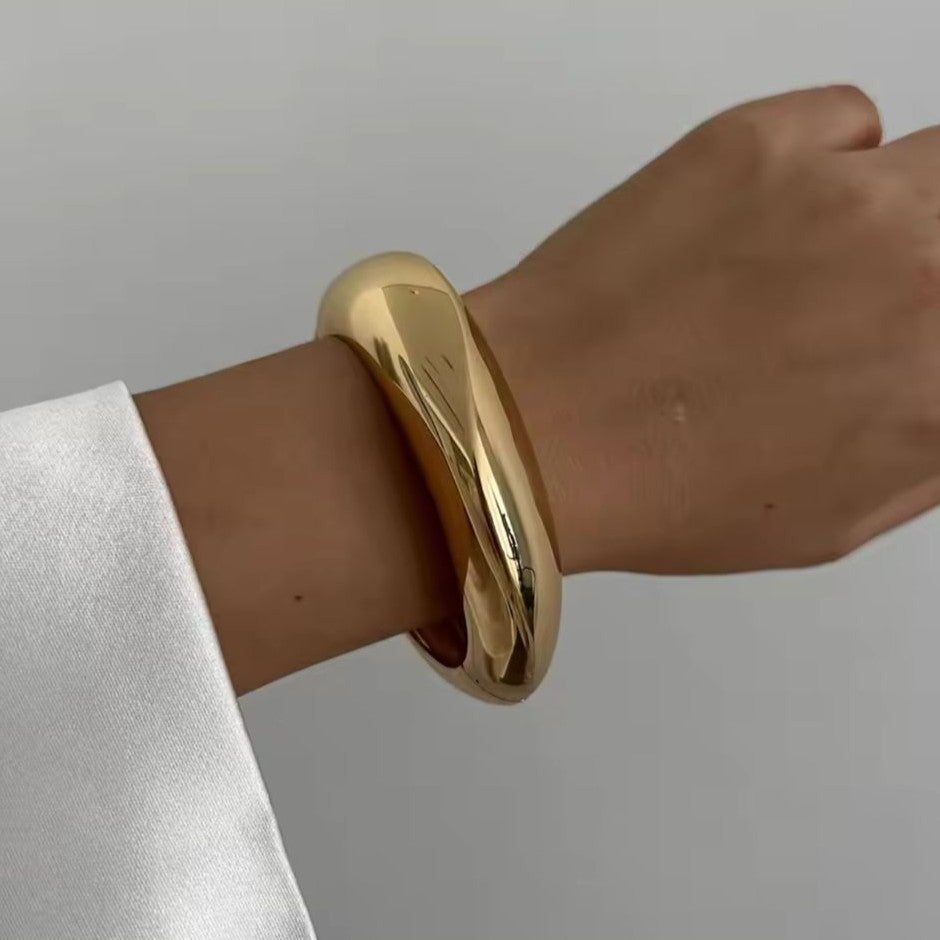 Gold bangle on a wrist with a plain background