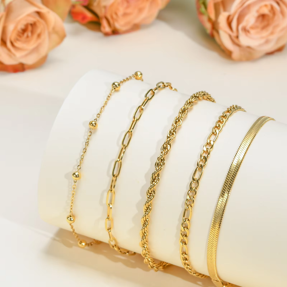 Set of gold bracelets on a white cushion with peach roses in the background