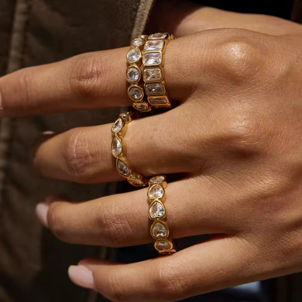 Close-up of a hand wearing multiple gold rings with gemstones on a blurred background