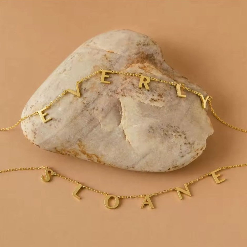 Gold name necklaces on a stone with a beige background