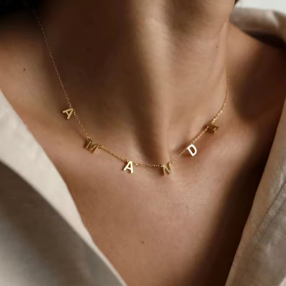 Gold necklace with 'AMANDA' letters on a person wearing a beige top.