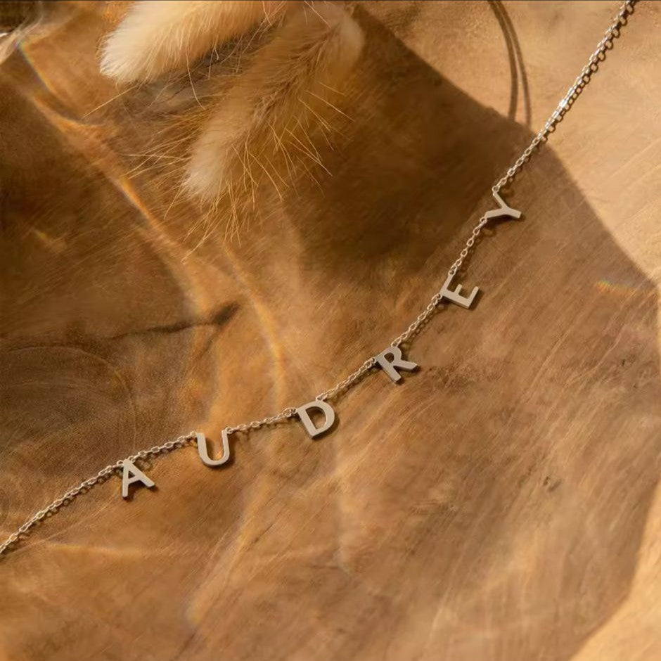 Necklace with 'AUDREY' letters on a wooden surface