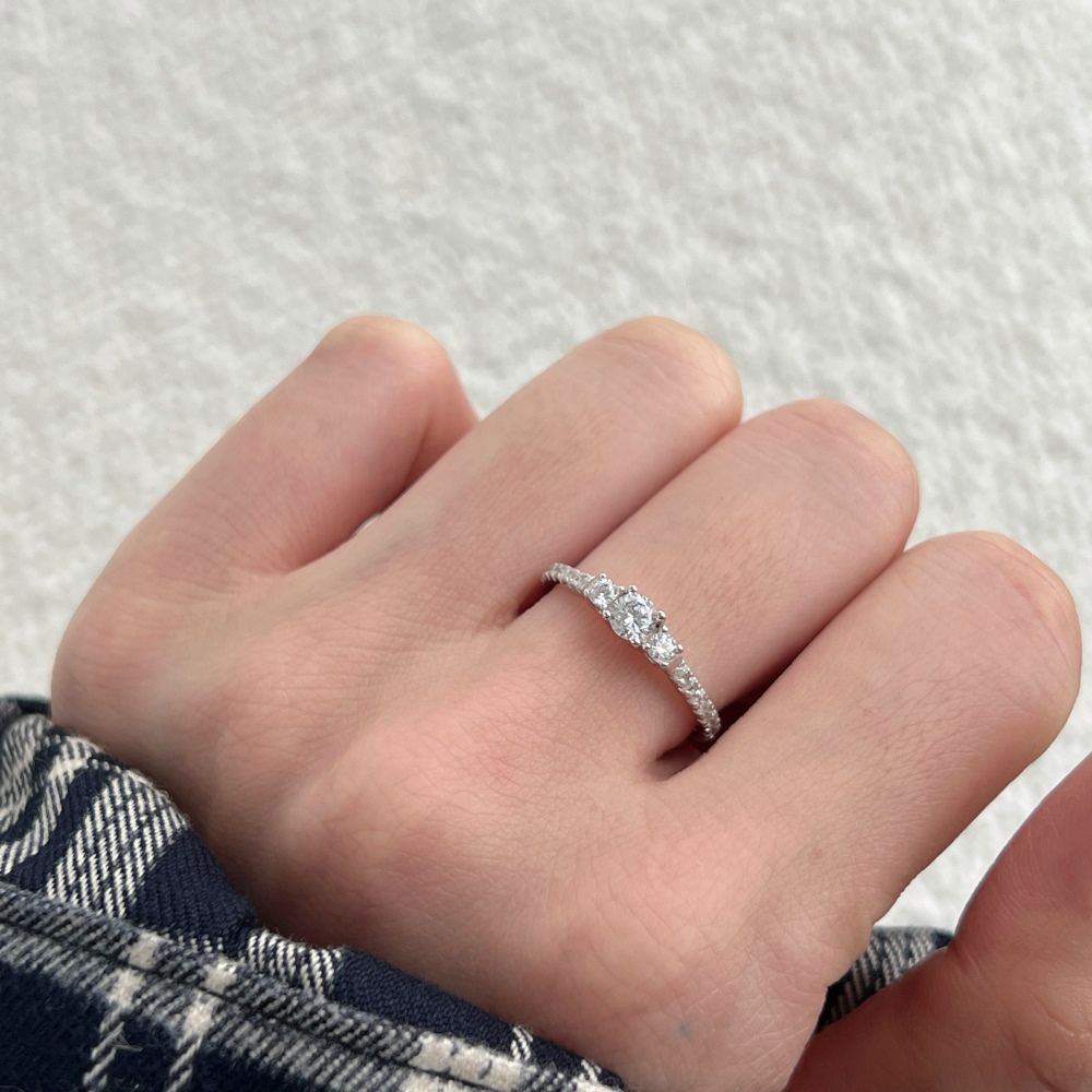 A dainty engagement ring featuring a central cubic zirconia stone with smaller stones on the band, set in a silver-tone mounting.