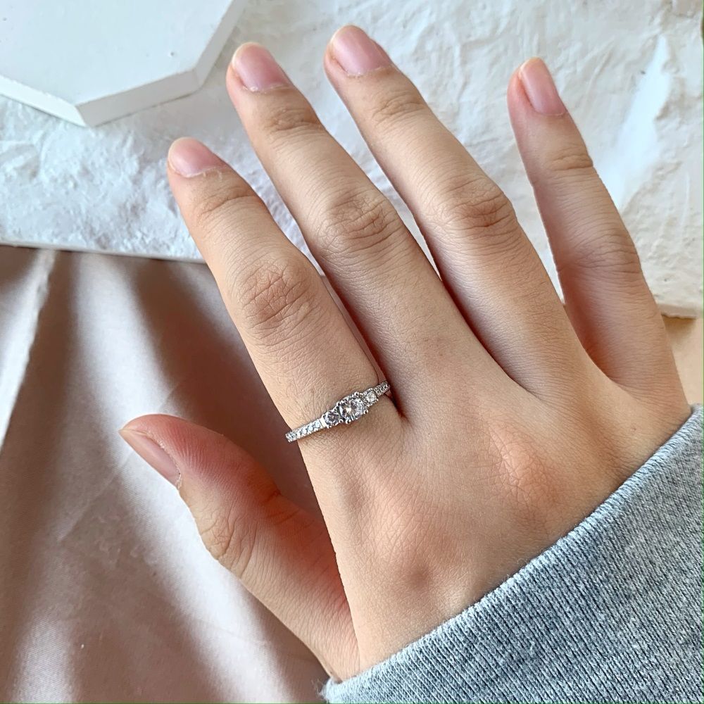 A dainty engagement ring featuring a central cubic zirconia stone with smaller stones on the band, set in a silver-tone mounting.